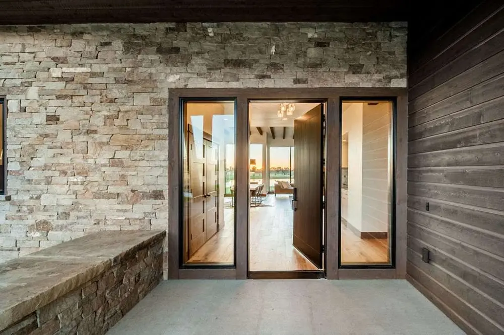 Modern home entrance with an open wood door, glass sidelights, and pale stone walls.